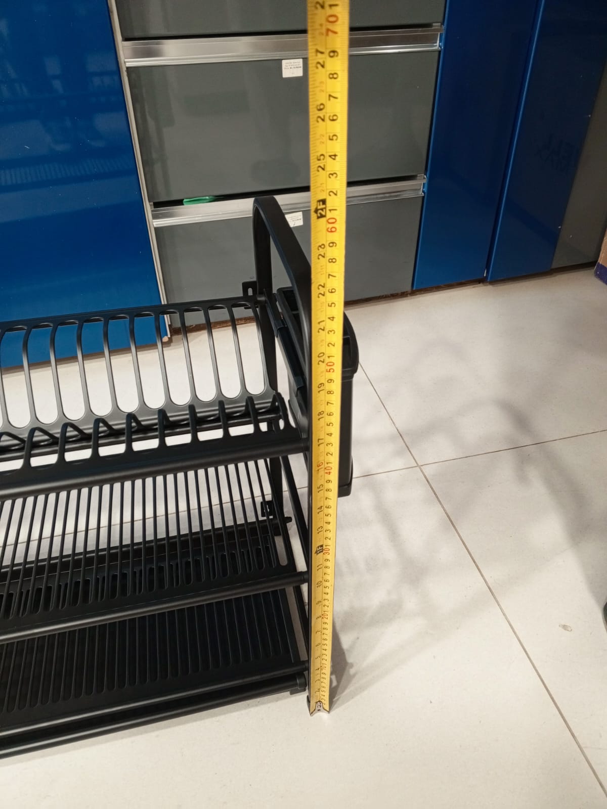 Black dish rack with a measuring tape for scale against a blue refrigerator.