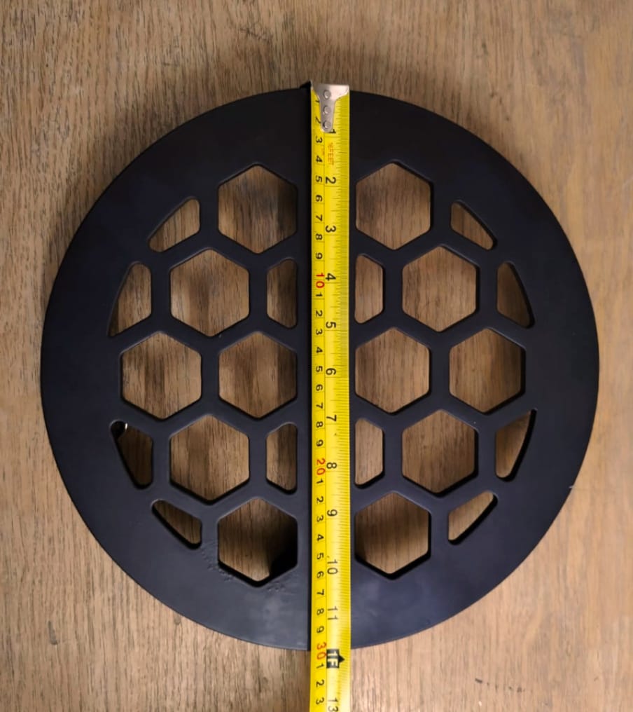 Round metal grating with honeycomb pattern on a wooden surface.